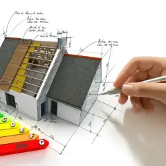 Projektowanie domów energooszczędnych: model domu z widocznym ociepleniem, schematem klasyfikacji energetycznej i ręką rysującą plany.