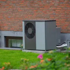 Solidny fundament pod pompę ciepła zapewnia stabilność urządzenia przy ceglanym murze domu.