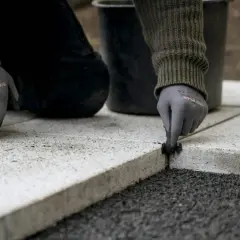 Ręce w rękawiczkach nakładają fugę do płyt tarasowych, tworząc trwałe i estetyczne połączenie.