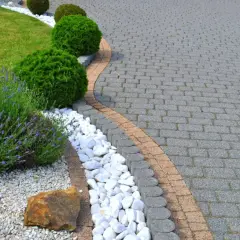 Ogród z zadbanym trawnikiem, kwitnącą lawendą i ozdobnymi krzewami. Wjazd z kostki brukowej, gdzie widoczna jest zmiana koloru kostki brukowej na granicy z rabatą.