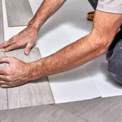 Ręce układają szary panel winylowy na białym podkładzie.