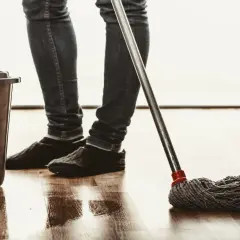 Osoba w jeansach i kapciach myje podłogę mopem, obok stoi wiadro. Naturalne czyszczenie octem.