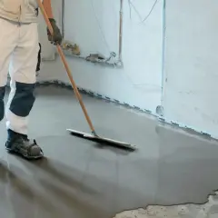 Pracownik w specjalnych butach rozprowadza masę samopoziomującą, idealną do tego, czym wyłożyć podłogę w piwnicy.