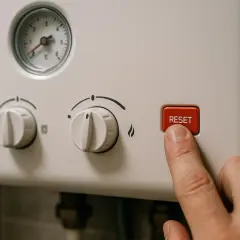 Palec naciska czerwony przycisk RESET na piecu CO, gdy słychać dziwne odgłosy.