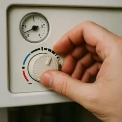 Dłoń kręci pokrętłem termostatu, pokazując jak ustawić piec gazowy dwufunkcyjny. Skala od czerwonego do niebieskiego sugeruje regulację temperatury.