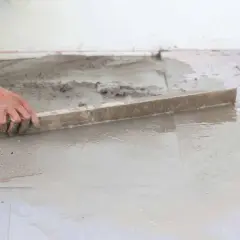Ręka wyrównuje świeży beton, tworząc idealną podłogę na gruncie.