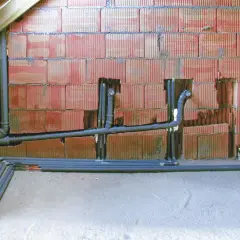 Instalacja odpowietrzenia kanału sanitarnego w domu parterowym. Rury PVC biegną wzdłuż ściany z pustaków ceramicznych.