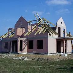 Budowa domu keramzytowego w różowym tynku, z widoczną konstrukcją dachu i wejściem z kolumnami.