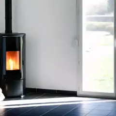 Nowoczesny piec na pellet z płomieniami, obok worek z pelletem. Codzienne wygaszanie pieca na pellet to rytuał.