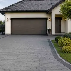 Tani podjazd do garażu z kostki brukowej, otoczony zadbanym ogrodem i zielenią.