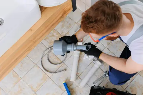 Instalator naprawia rury pod umywalką, prawdopodobnie z powodu braku odpowietrzenia pionu.