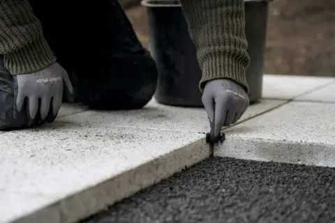 Ręce w rękawiczkach nakładają fugę do płyt tarasowych, tworząc trwałe i estetyczne połączenie.