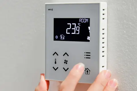 Dłoń dotyka panelu sterownika do powietrznej pompy ciepła, wyświetlającego 23.9°C.