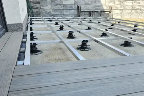 Budowa tarasu z deski kompozytowej. Widoczna konstrukcja nośna z aluminiowych profili i regulowanych podpór.