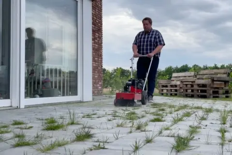 Mężczyzna używa maszyny do czyszczenia kostki brukowej, pokazując, jak usunąć mech z kostki.