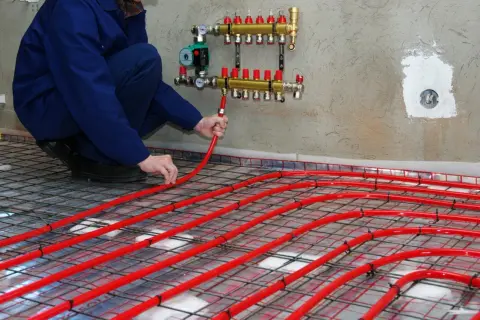 Instalator układa rury podłogówki, dobierając odpowiedni rozdzielacz do ogrzewania 100m2.