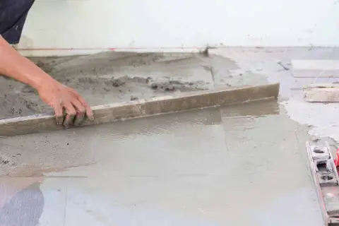 Ręka wyrównuje świeży beton, tworząc idealną podłogę na gruncie.