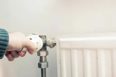 Dłoń reguluje termostat grzejnika, przygotowując się do odpowietrzenia grzejnika żeliwnego.