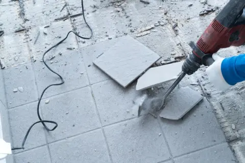 Skuwanie płytek młotem udarowym. Widać kurz i fragmenty materiału.