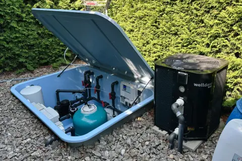 System do podgrzewania wody w basenie: pompa ciepła obok niebieskiej skrzyni z filtrem i instalacją hydrauliczną.
