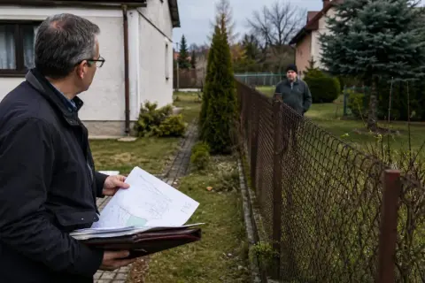 Mężczyzna z dokumentami analizuje sytuację z płotem sąsiada na mojej działce, być może w kontekście zasiedzenia.
