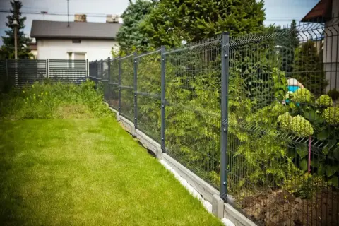 Nowy, nowoczesny płot panelowy oddziela zadbany trawnik od zieleni. Czy można postawić płot przy płocie? Tak, jeśli sąsiad ma taki sam!