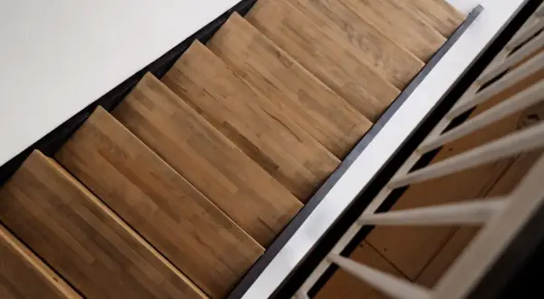 Drewniane schody z paneli laminowanych, z czarną metalową konstrukcją i białymi poręczami, prowadzą w górę.