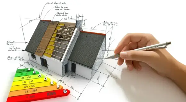 Projektowanie domów energooszczędnych: model domu z widocznym ociepleniem, schematem klasyfikacji energetycznej i ręką rysującą plany.