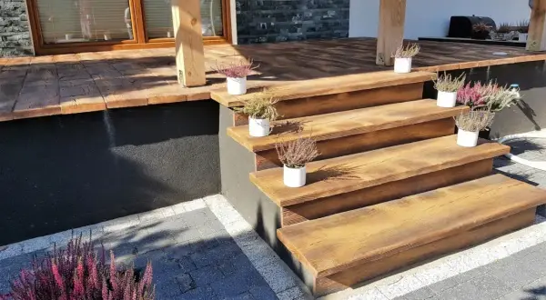 Drewniane schody i taras z kostki brukowej. Idealne rozwiązanie, czym wyłożyć taras, by wyglądał naturalnie i stylowo.