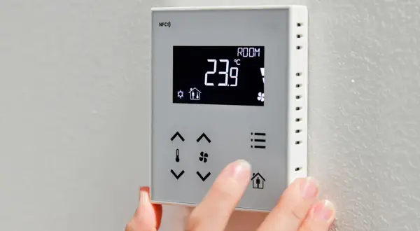 Dłoń dotyka panelu sterownika do powietrznej pompy ciepła, wyświetlającego 23.9°C.