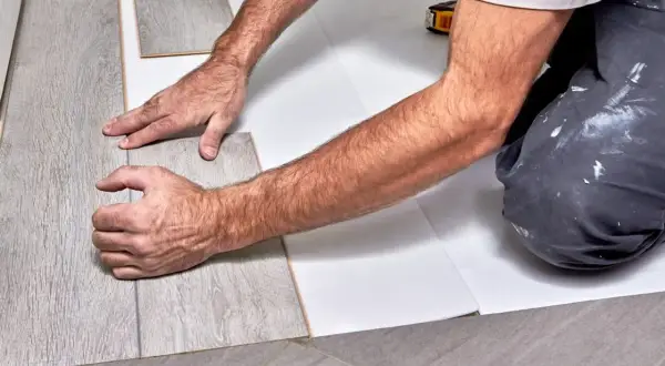 Ręce układają szary panel winylowy na białym podkładzie.