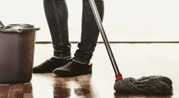 Osoba w jeansach i kapciach myje podłogę mopem, obok stoi wiadro. Naturalne czyszczenie octem.