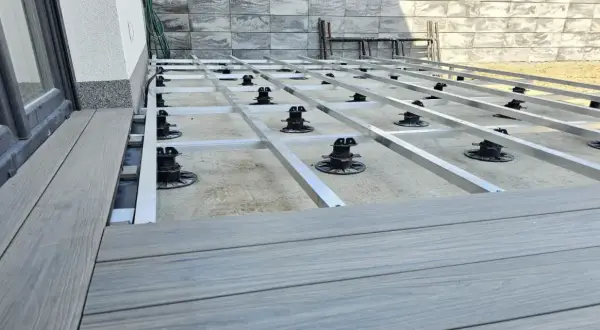 Budowa tarasu z deski kompozytowej. Widoczna konstrukcja nośna z aluminiowych profili i regulowanych podpór.