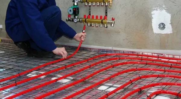 Instalator układa rury podłogówki, dobierając odpowiedni rozdzielacz do ogrzewania 100m2.