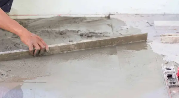 Ręka wyrównuje świeży beton, tworząc idealną podłogę na gruncie.