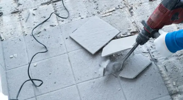 Skuwanie płytek młotem udarowym. Widać kurz i fragmenty materiału.