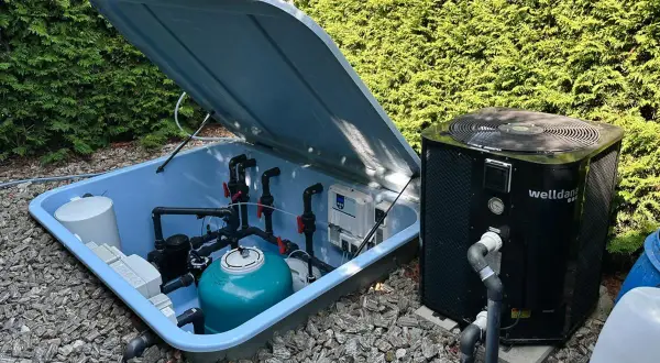 System do podgrzewania wody w basenie: pompa ciepła obok niebieskiej skrzyni z filtrem i instalacją hydrauliczną.