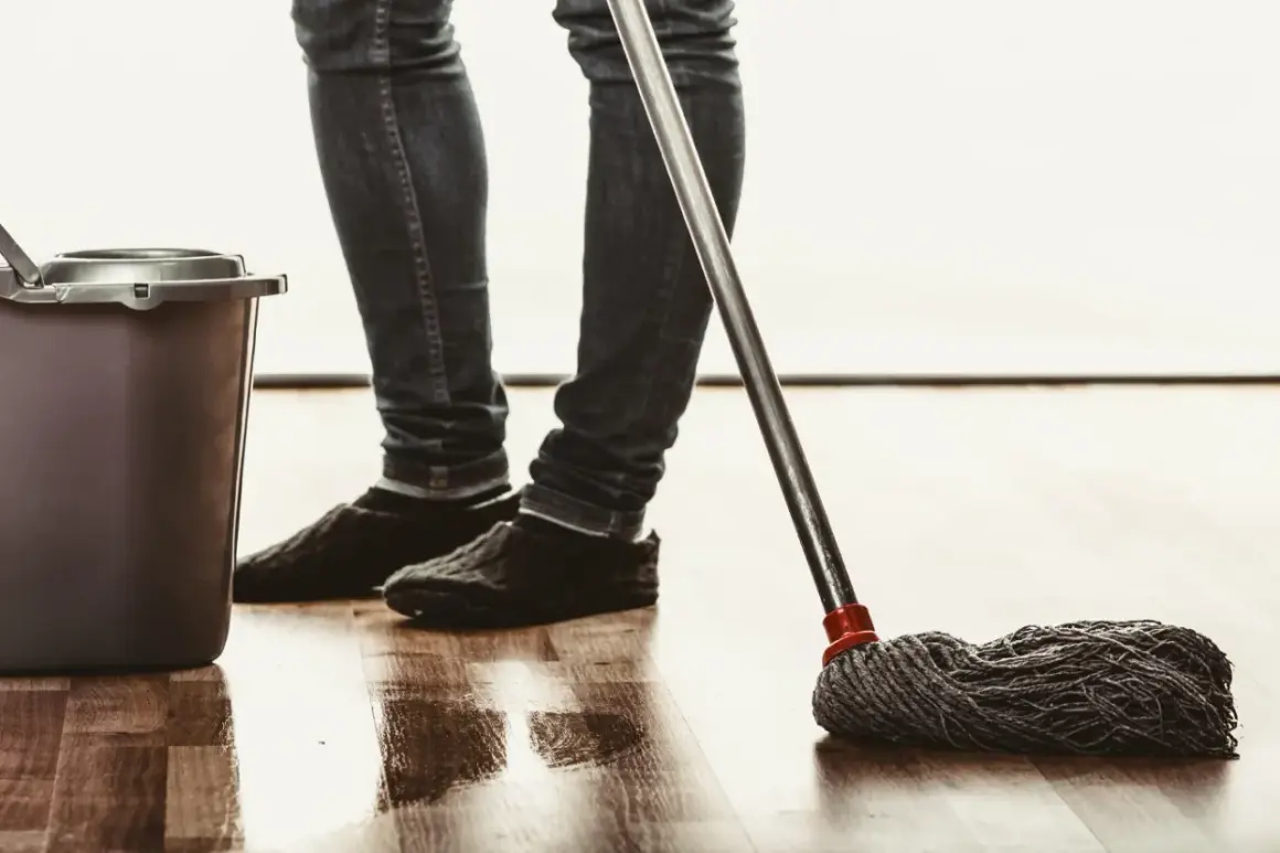Osoba w jeansach i kapciach myje podłogę mopem, obok stoi wiadro. Naturalne czyszczenie octem.