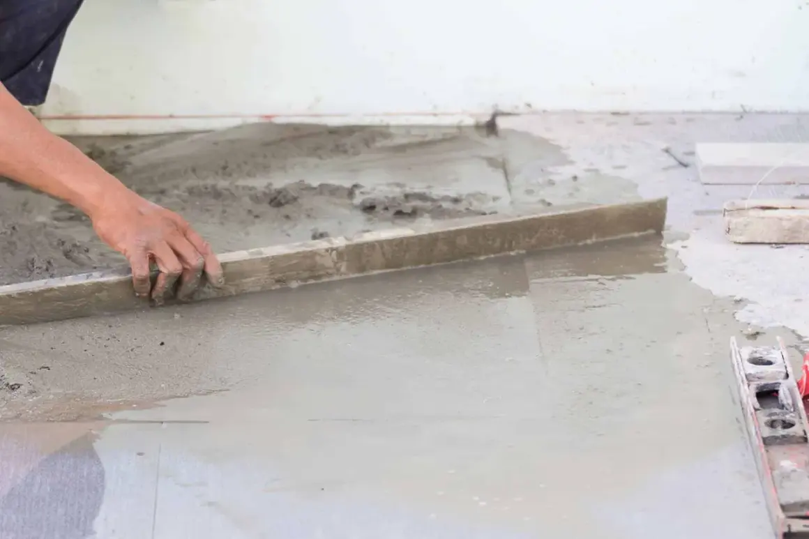 Ręka wyrównuje świeży beton, tworząc idealną podłogę na gruncie.