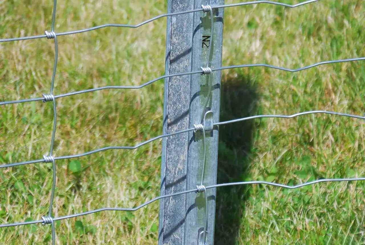 Detale montażu siatki ogrodzeniowej na metalowym słupku. Druty połączone z słupkiem.