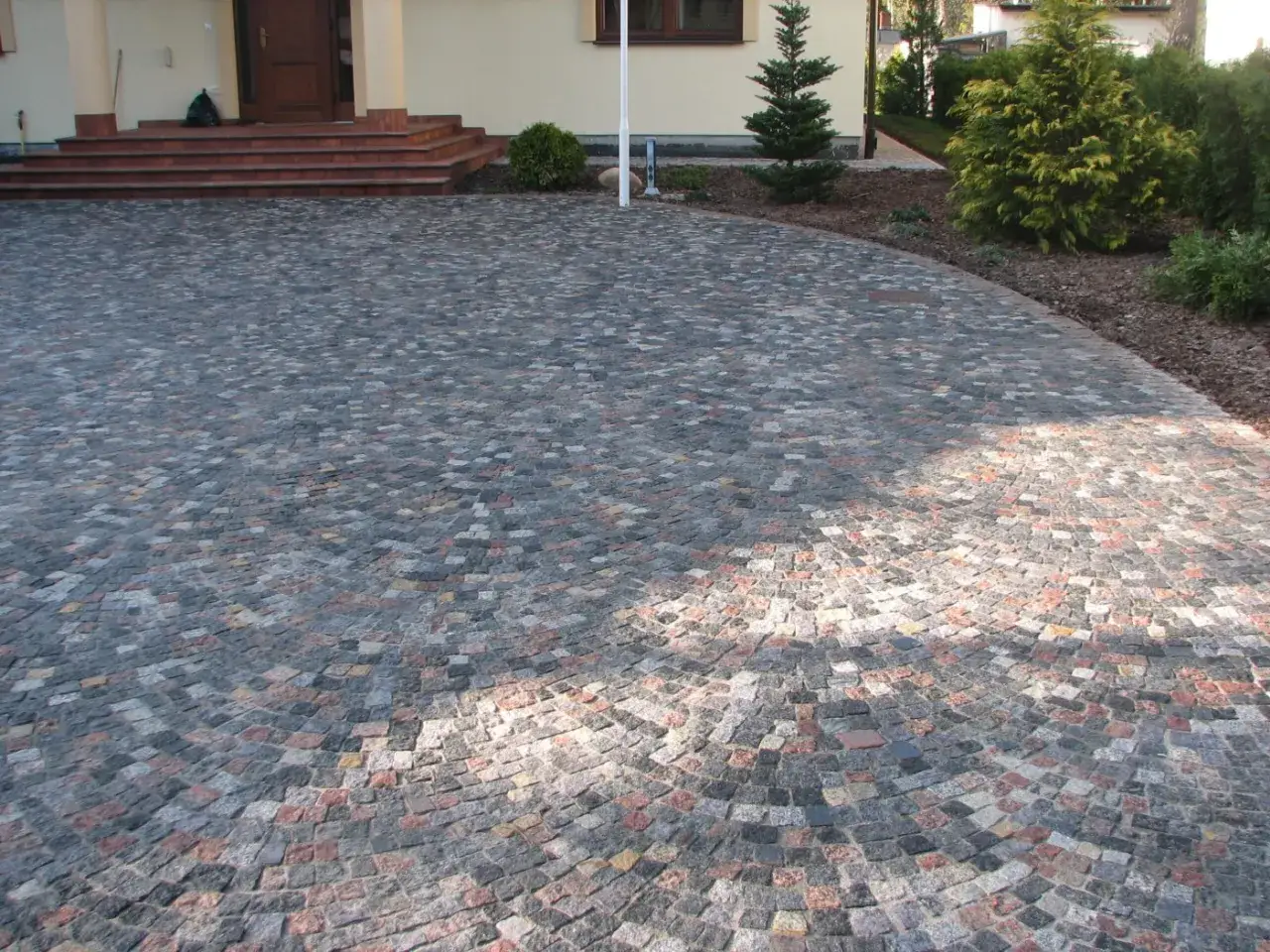 Piękny podjazd z kamienia, ułożony w łuk, prowadzi do drzwi domu. Kamienne kostki tworzą mozaikę w odcieniach szarości i czerwieni.