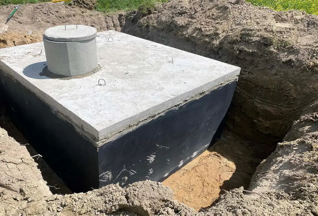 Betonowe szambo w wykopie, gotowe do zasypania. Warto pamiętać o wapnie do szamba dla lepszej stabilizacji.