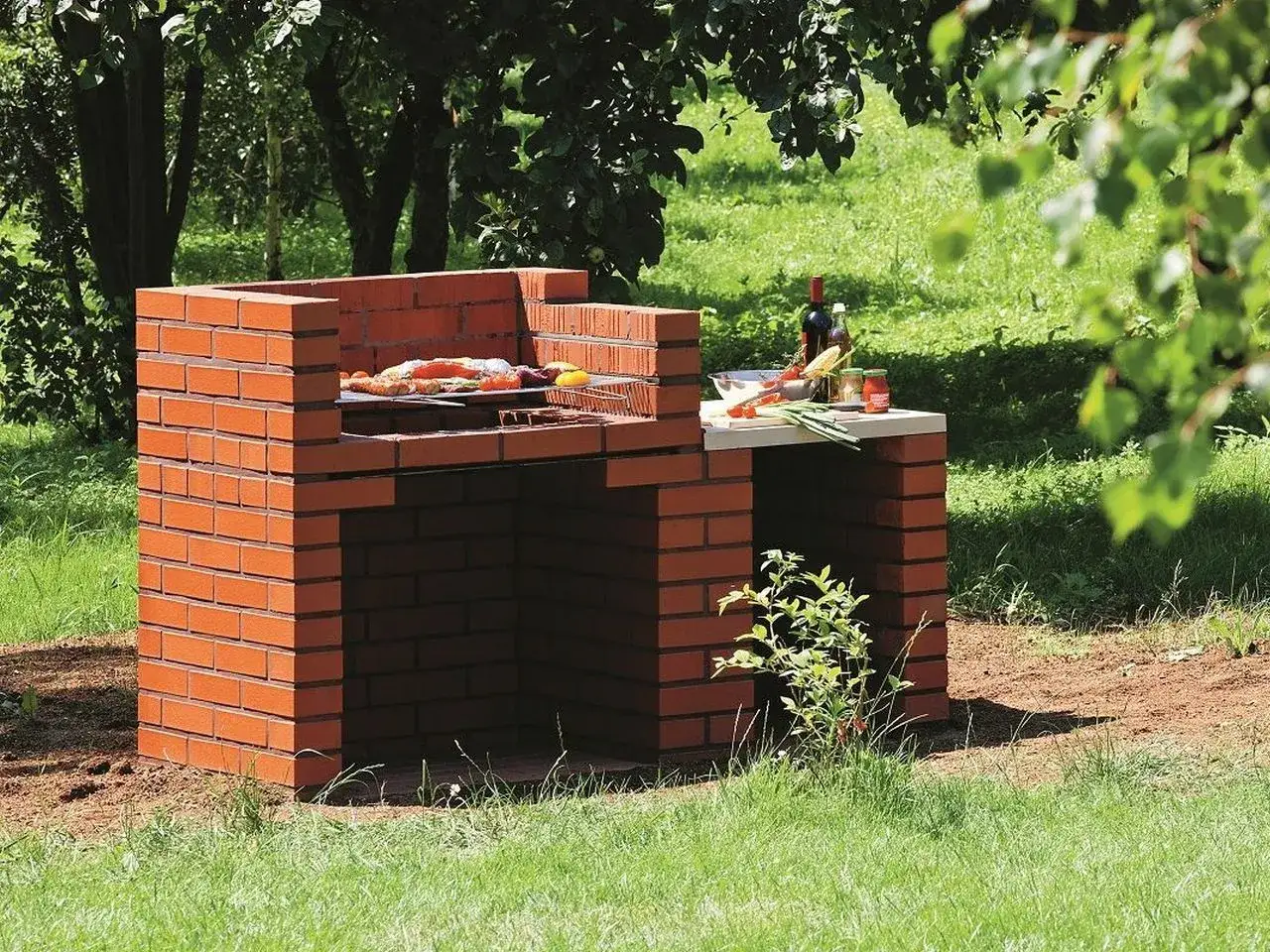 Solidny grill murowany gotowy na letnie przyjęcie. Na ruszcie już czeka pyszne jedzenie, a obok butelka wina i warzywa.