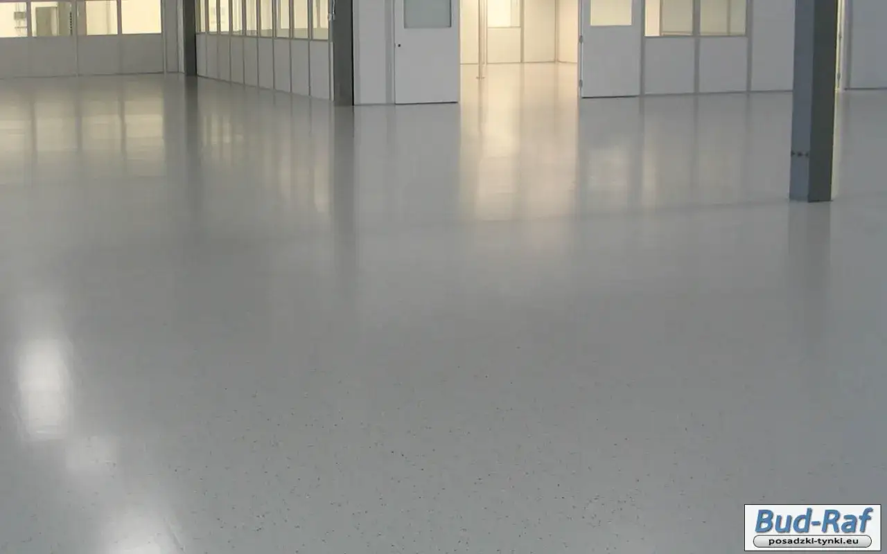 Gładka, jasnoszara posadzka betonowa z drobnymi, ciemnymi wtrąceniami. Idealne rozwiązanie, gdy zastanawiasz się, jak wyrównać posadzkę betonową.