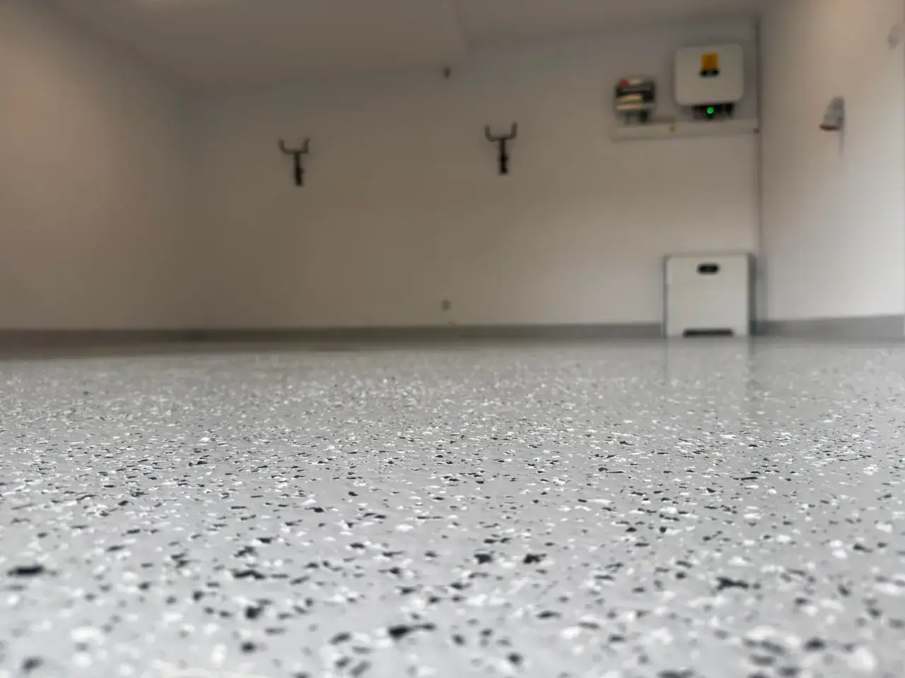 Nowa, lśniąca podłoga epoksydowa w garażu, z widocznymi elementami technicznymi na ścianie.