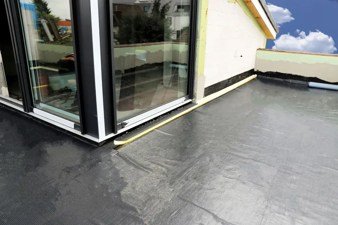 Nowy balkon z czarną membraną, zapewniającą skuteczną hydroizolację balkonu. Widoczny fragment okna i ściany budynku.