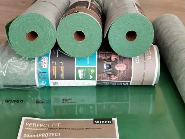Rolki zielonego podkładu pod panele, idealne do ogrzewania podłogowego. Materiał "Perfect Fit" od wineo zapewnia komfort i izolację.