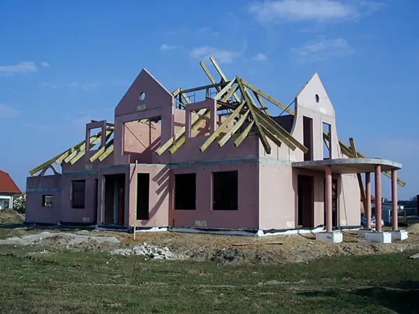 Budowa domu keramzytowego w różowym tynku, z widoczną konstrukcją dachu i wejściem z kolumnami.