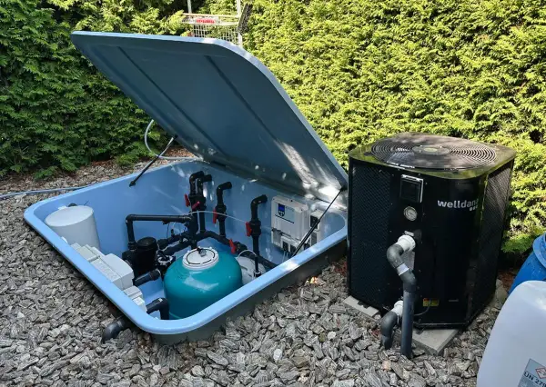System do podgrzewania wody w basenie: pompa ciepła obok niebieskiej skrzyni z filtrem i instalacją hydrauliczną.
